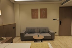Quarto de hotel com um sofá cinzento, uma mesa redonda pequena e duas pinturas abstratas na parede.