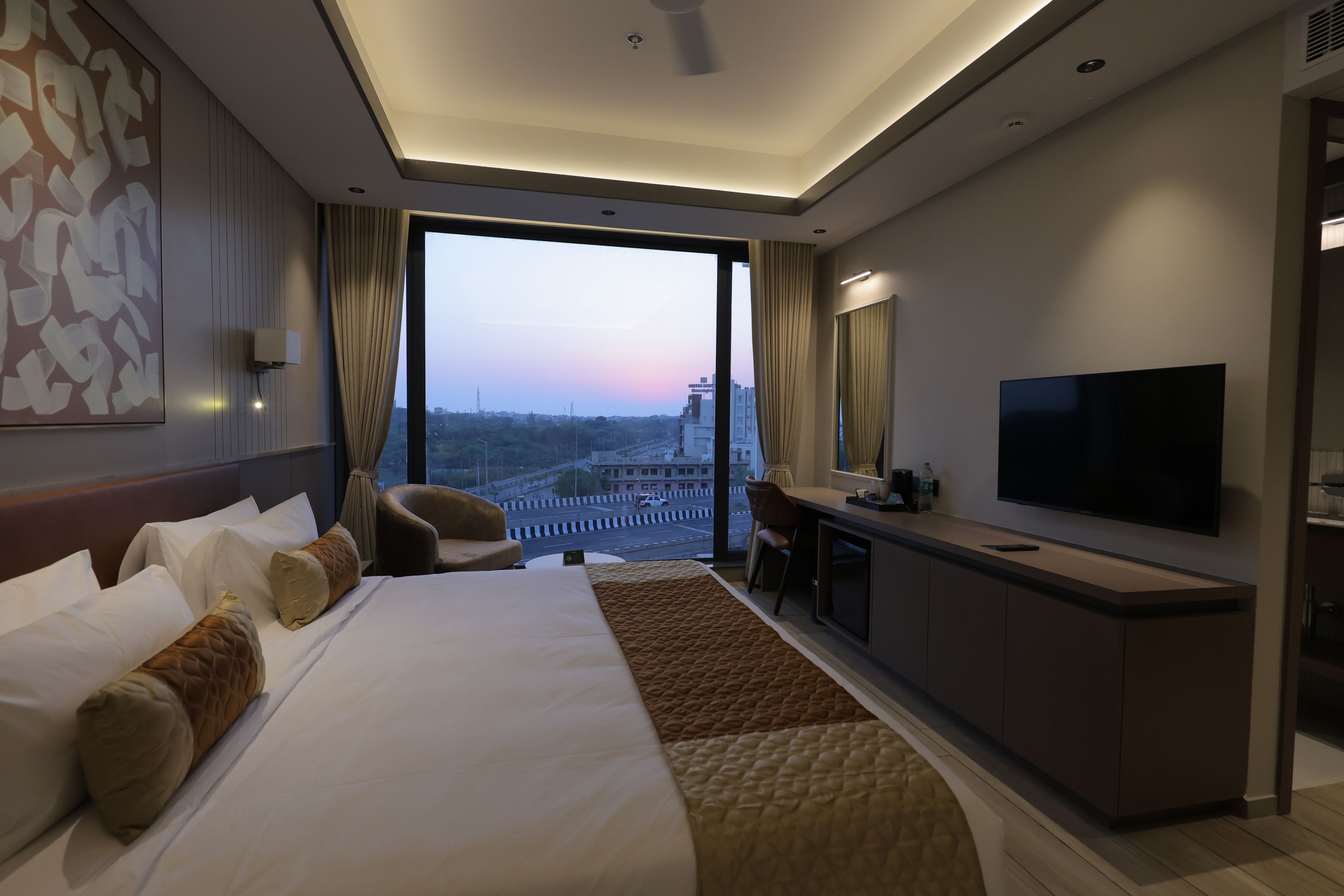 Ett modernt hotellrum med en stor säng, ett skrivbord, en tv och utsikt över stadsbilden.