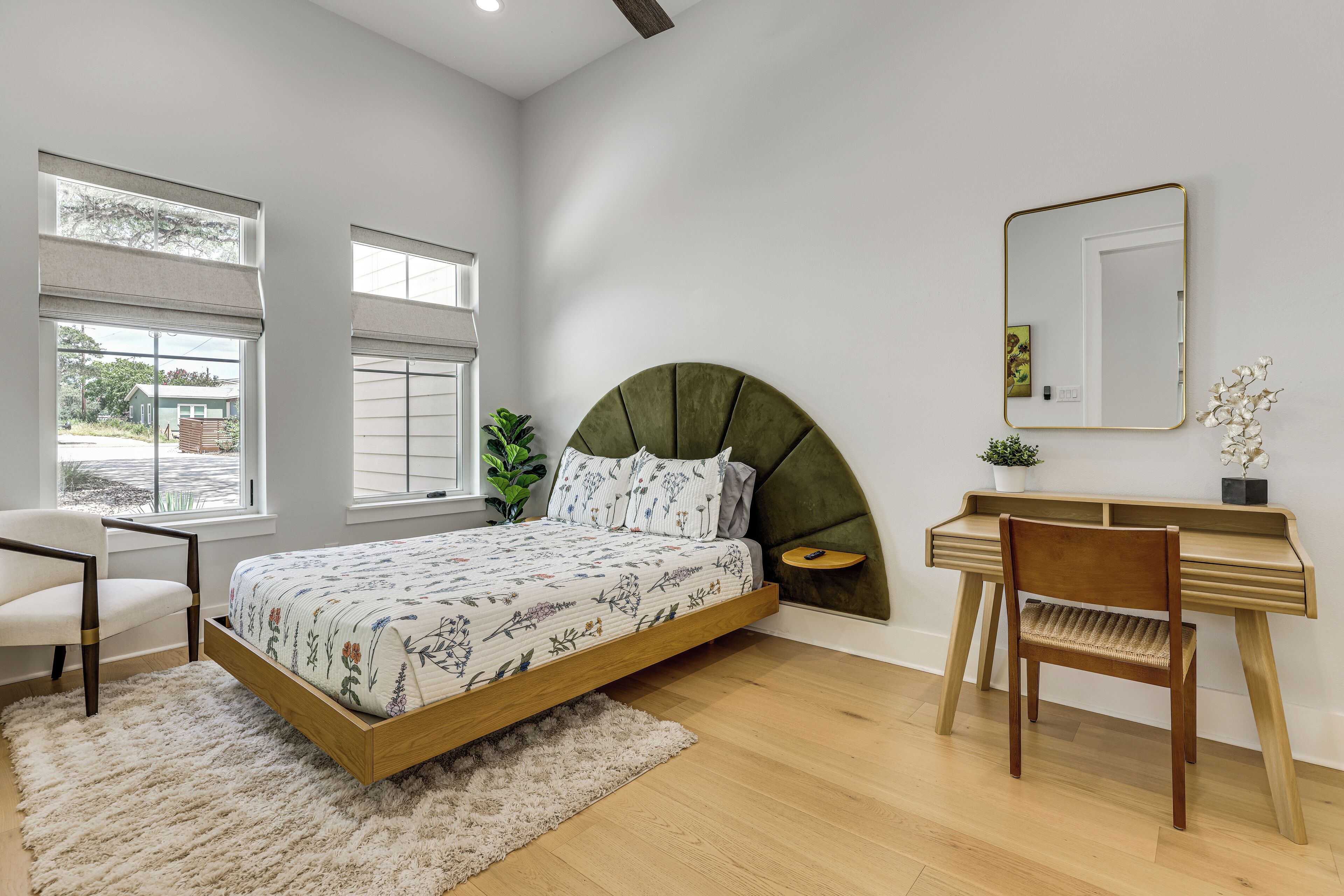 A bedroom with a bed, a desk, a chair, a mirror, and a window.
