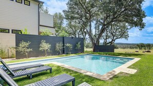 Un área de piscina moderna con sillones de descanso, una alberca y un árbol grande.