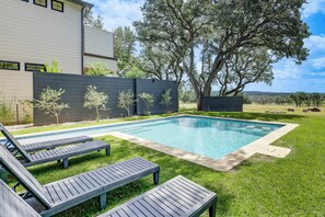 Ein moderner Poolbereich mit Liegestühlen, einem Schwimmbecken und einem großen Baum.