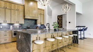 Una cocina moderna con armarios de madera, una isla de mármol, taburetes de bar e iluminación colgante.
