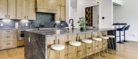 Una cocina moderna con armarios de madera, una isla de mármol, taburetes de bar e iluminación colgante.