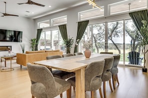 A spacious dining area with a wooden table and chairs, a sofa, and large windows with curtains. - Pool & Lake Access! Dual Homes on Canyon Lake (Canyon Lake)