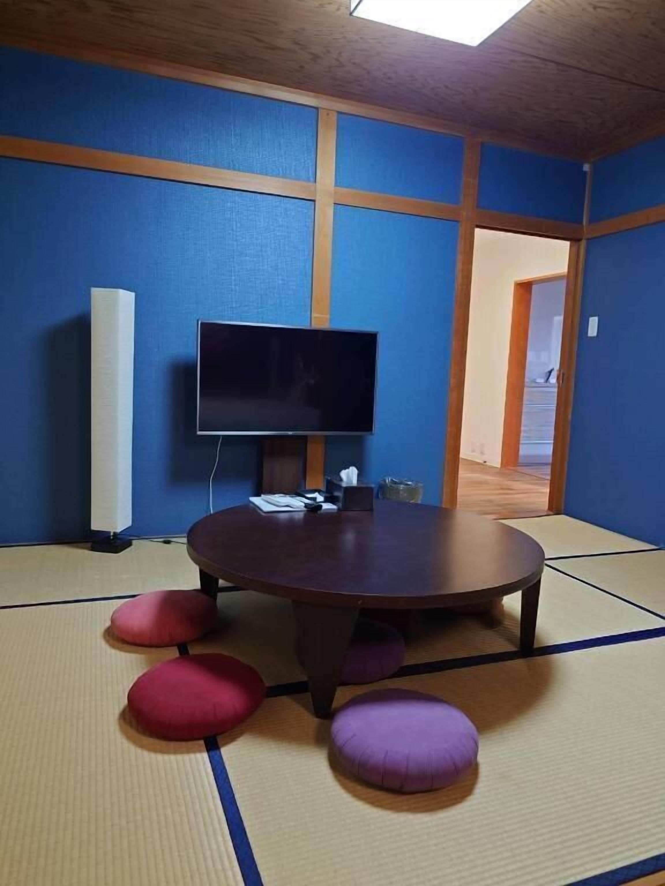 A room with tatami flooring, a round table, and a flat-screen TV.