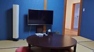 A room with tatami flooring, a round table, and a flat-screen TV.