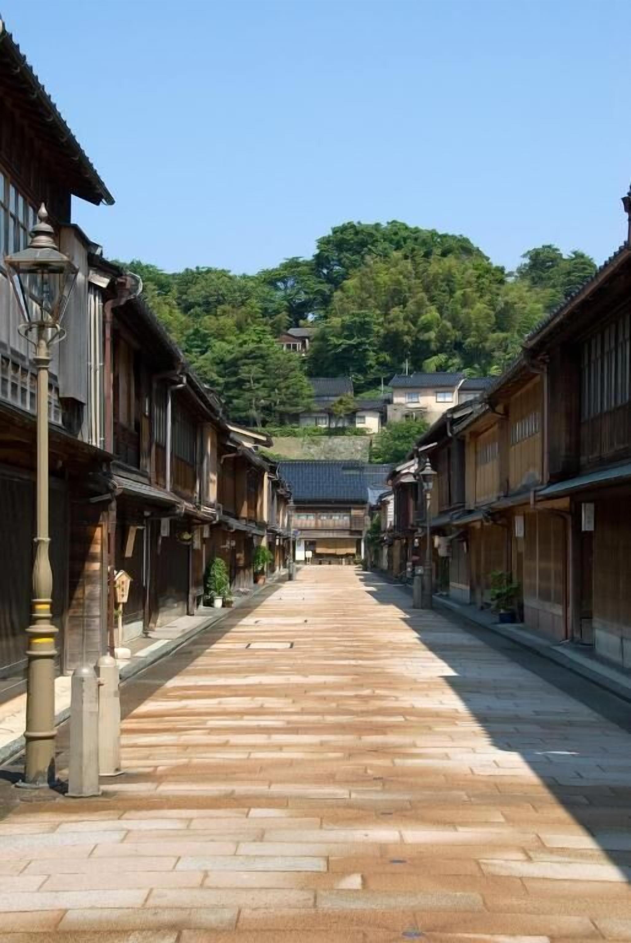 A traditional Japanese street with wooden buildings, a clear sky, and a hill in the background.