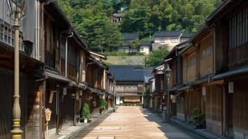 A traditional Japanese street with wooden buildings, a clear sky, and a hill in the background.