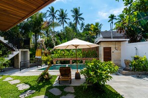 Un espace piscine doté d’une terrasse en bois, d’une chaise longue et d’un grand parasol.