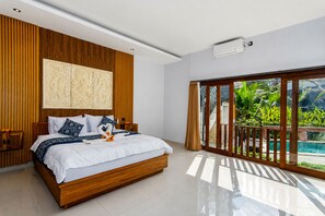 Une chambre moderne avec une tête de lit en bois, un grand lit avec une literie blanche et des coussins décoratifs, une grande fenêtre donnant sur une piscine et un espace verdoyant, et un appareil de climatisation fixé au plafond.