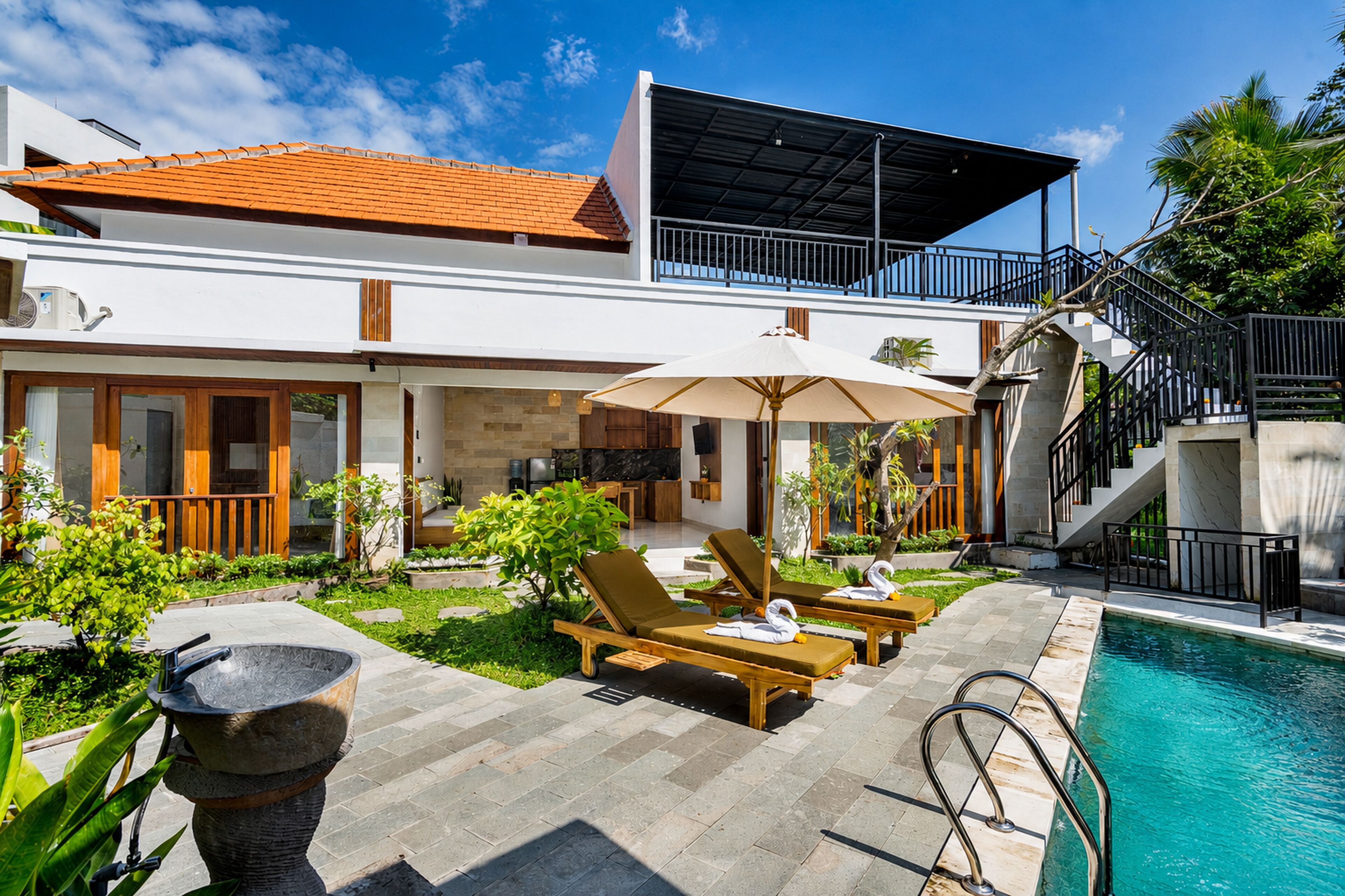 Una casa moderna de dos pisos con piscina, mobiliario exterior y una escalera que lleva a un balcón.