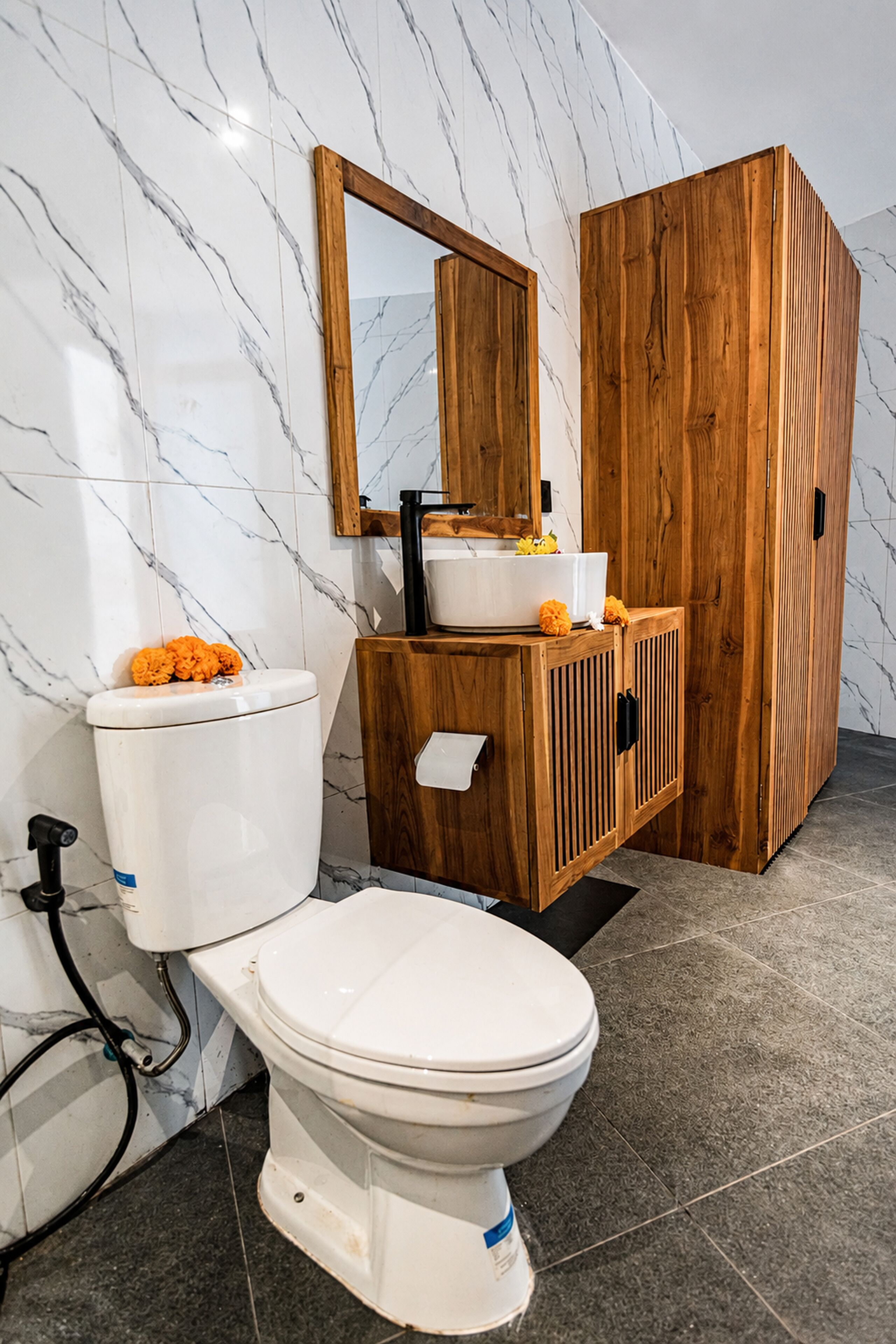 A bathroom with a toilet, a wooden cabinet, and a marble wall.