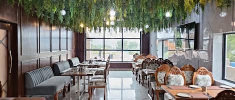 A restaurant with long communal tables and benches, a high ceiling with hanging greenery, and large windows.