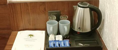 A hotel room's breakfast setup with a menu, two cups, a kettle, and some packaged food items.