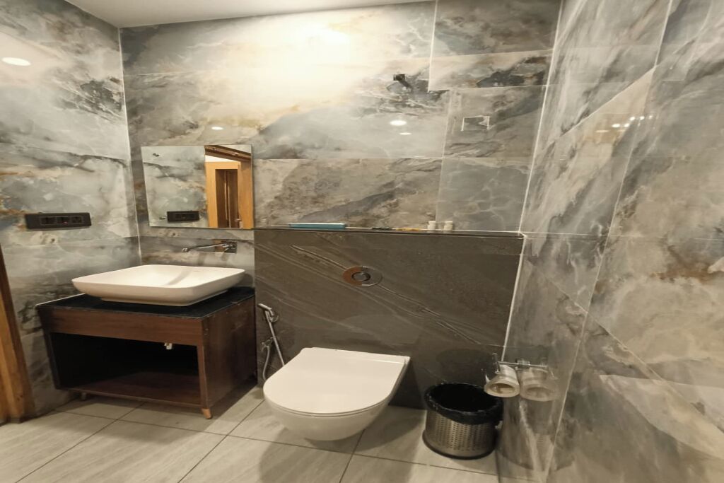 A bathroom with a marble wall, a sink, a toilet, and a mirror.