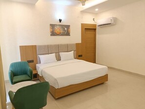 Habitación de hotel con cama, dos sillas, aire acondicionado montado en la pared y una puerta.