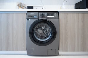 A front view of a modern washing machine with a control panel, set against a wooden cabinet backdrop.