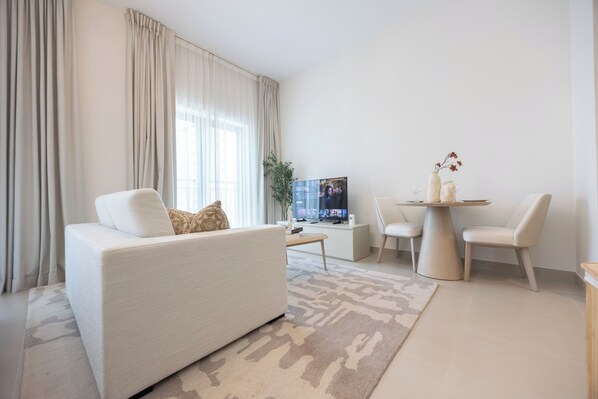 A modern living room with a sofa, a coffee table, a TV, and a dining area with chairs and a small table.