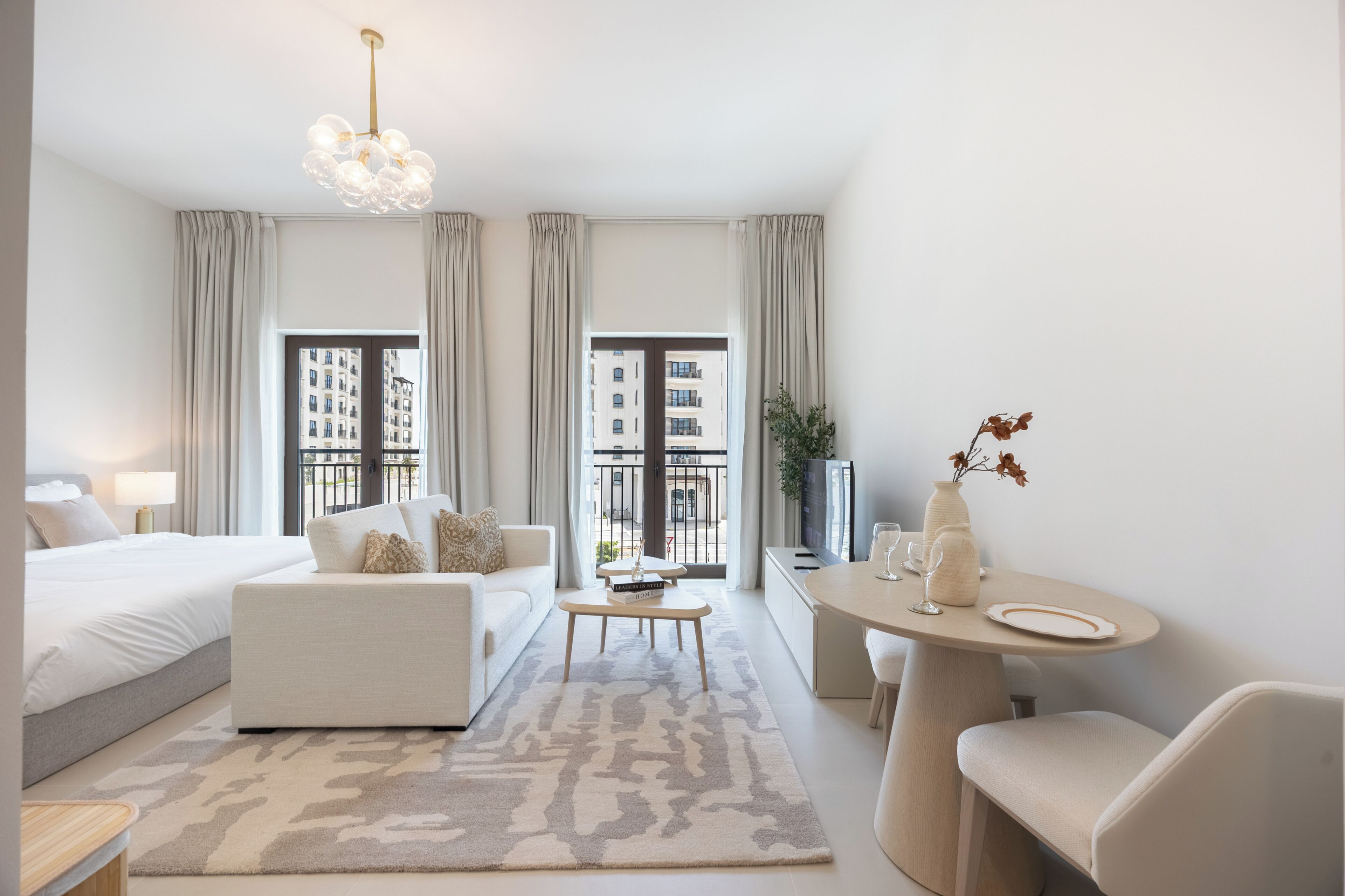 Una habitación de hotel moderna con cama, sofá, mesa de centro y zona de comedor con mesa y sillas.