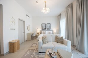 A modern hotel room with a sofa, a desk, a bed, and a chandelier.