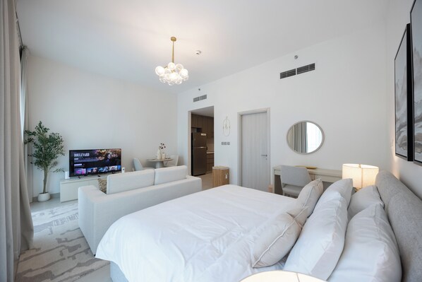 A modern hotel room with a large bed, a television, a dining area, and a bathroom.