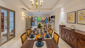 Un comedor con una mesa larga dispuesta para cuatro personas, una araña y vista a la cocina.