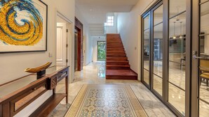 Un interior moderno con una escalera de madera, piso de mármol y un cuadro abstracto grande.