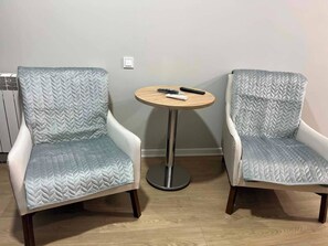 Zwei Sessel mit Strukturmuster, ein kleiner runder Tisch mit Fernbedienung und ein Lichtschalter an der Wand.