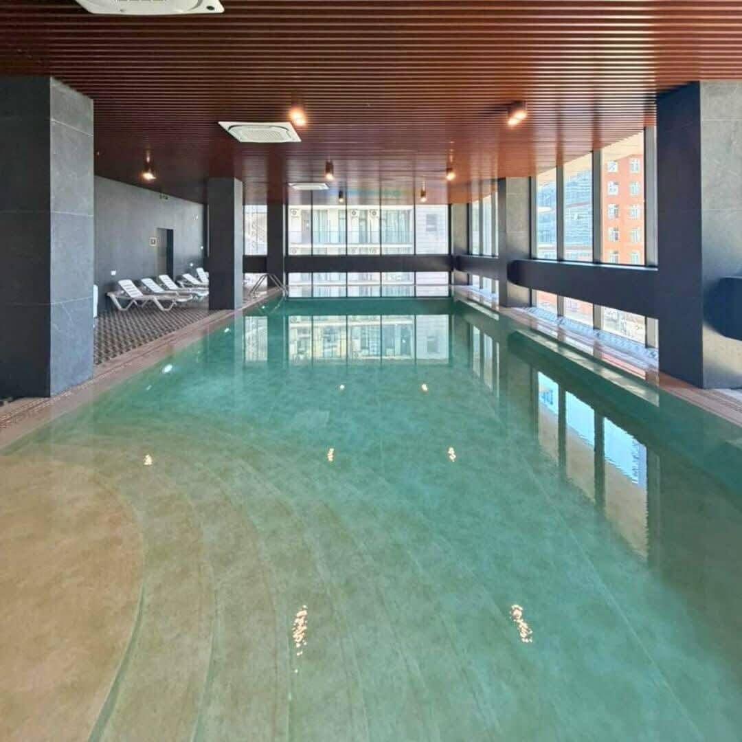 Une piscine intérieure avec des parois en verre transparent, un sol carrelé et des luminaires au plafond.