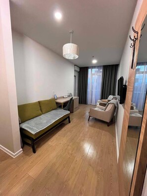A modern, well-lit room with a sofa, a small table, a chair, and a bed. - Modern 1BR Seaside Apartment, Walk to the Beach (Batumi)