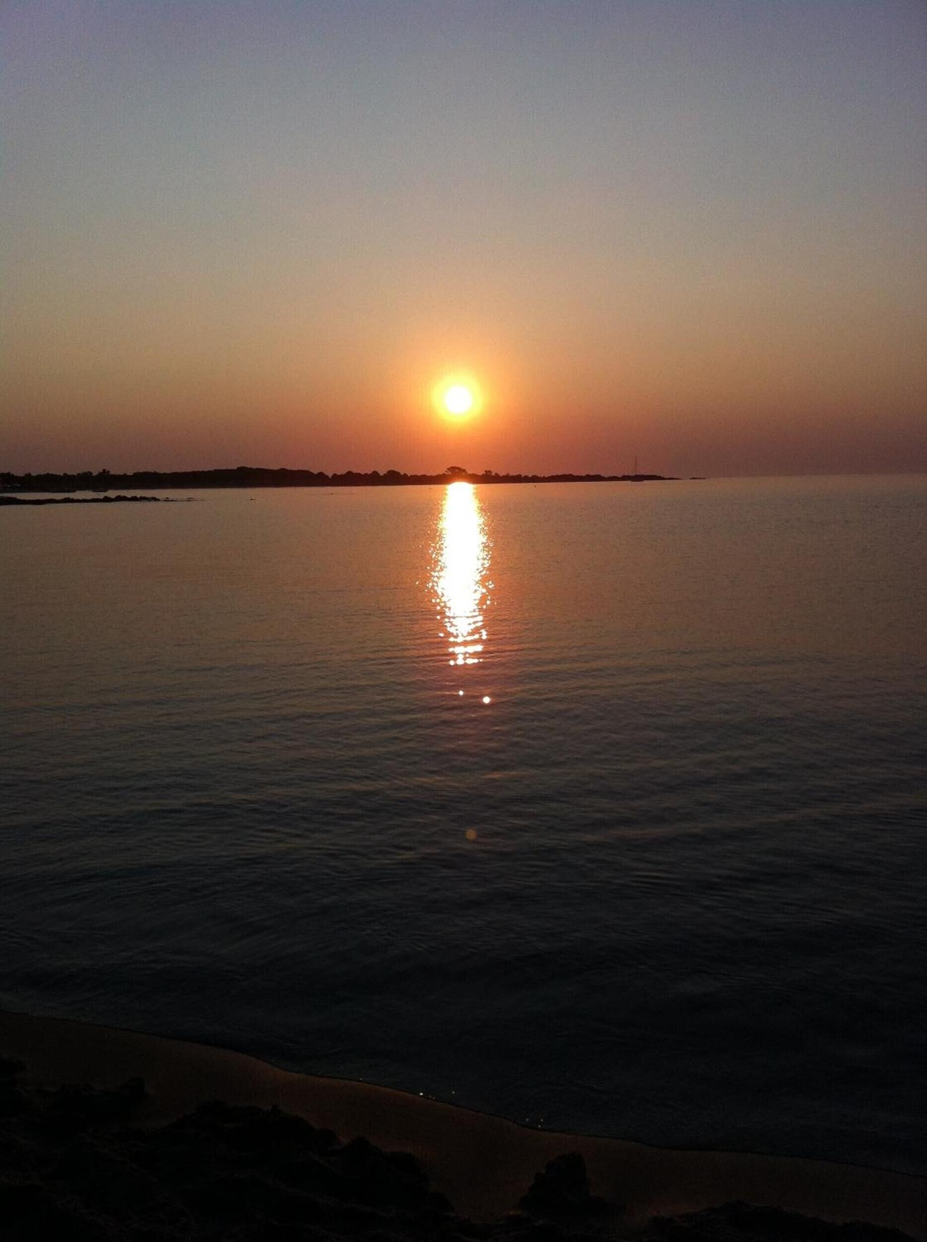 Solnedgang over rolige vandflader med en fjerntliggende kystlinje.