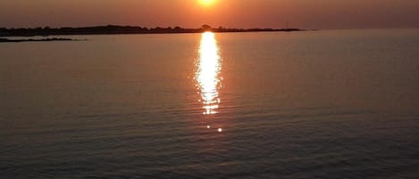 A sunset over a calm body of water with a distant shoreline.
