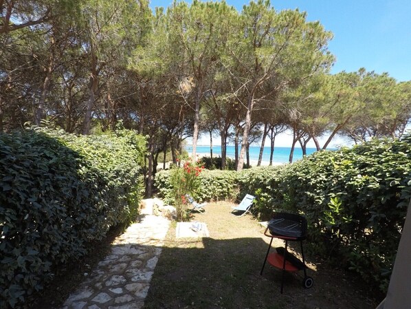A garden with a stone pathway leading to a barbecue area, surrounded by dense foliage and trees.