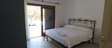 Un dormitorio con cama, una puerta y vista a través de un ventanal.