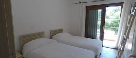 A room with two beds, a sliding glass door leading to a balcony, and an air conditioning unit on the wall.
