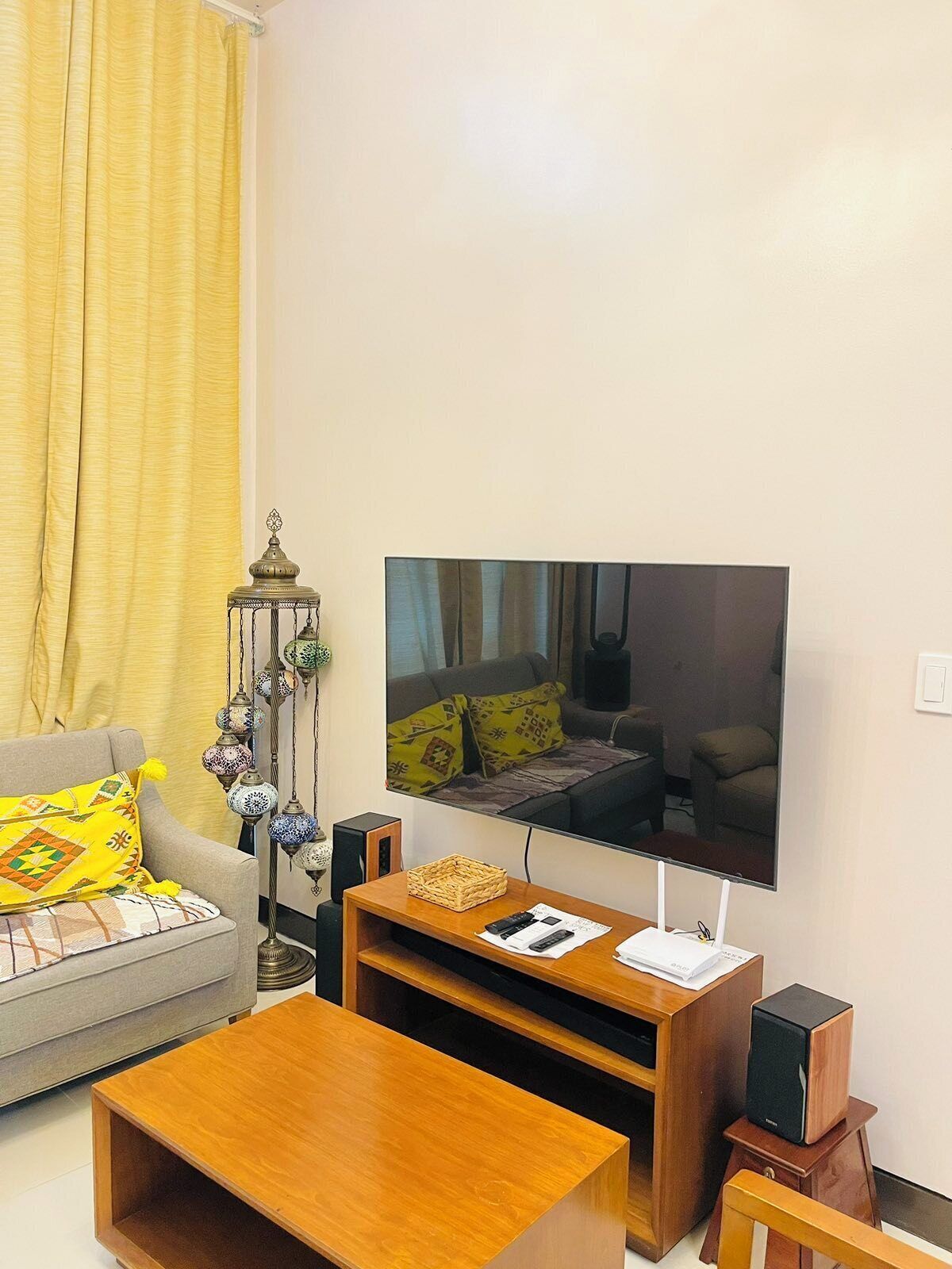Una sala de estar con televisor de pantalla plana, un sofá, una mesa de centro y una lámpara decorativa.