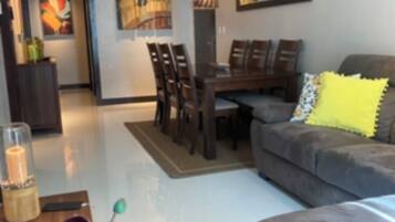 Uma sala de estar moderna com um sofá cinzento, uma mesa de jantar com cadeiras e uma mesa de centro com um vaso de flores.