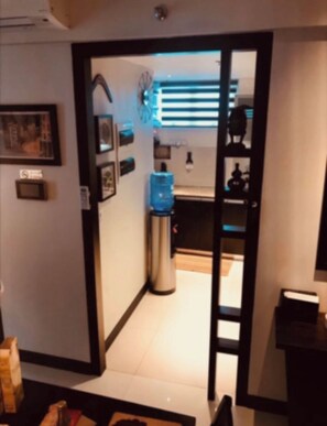 A hallway leading to a kitchen with a water dispenser, a microwave, and framed pictures on the wall.