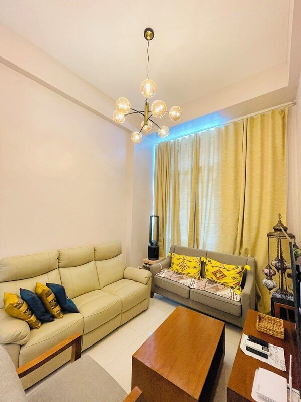 A living room with a beige sofa, a wooden coffee table, and a modern chandelier. - MactanRent.ph (Lapu-Lapu)