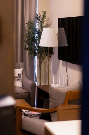 A modern living room with a sofa, a coffee table, a floor lamp, a television, and a large plant.