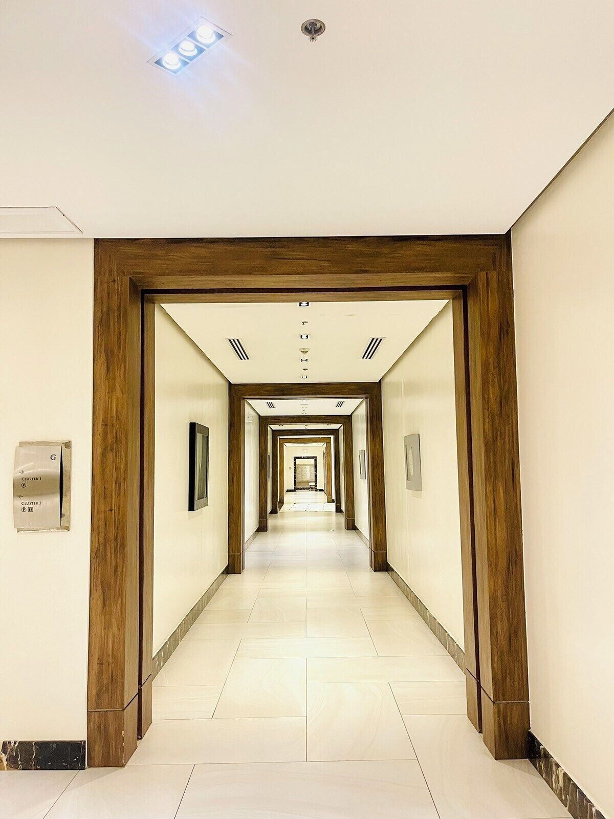 A hotel corridor with a wooden frame, a sign indicating cluster G, and a tiled floor.