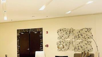 A modern lobby with a seating area, a large abstract wall art piece, and a door with a dark frame.