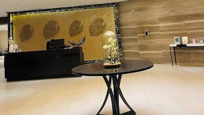 A reception area with a modern chandelier, a reception desk, and a wall with leaf patterns.