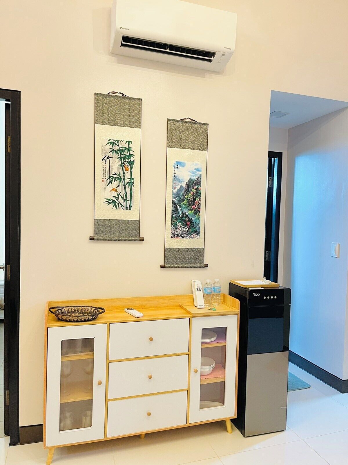 A room with a white cabinet with glass doors, a black dishwasher, and two vertical paintings on the wall.