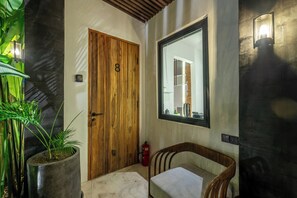 A wooden door with a number, a potted plant, a chair, and a wall-mounted mirror.