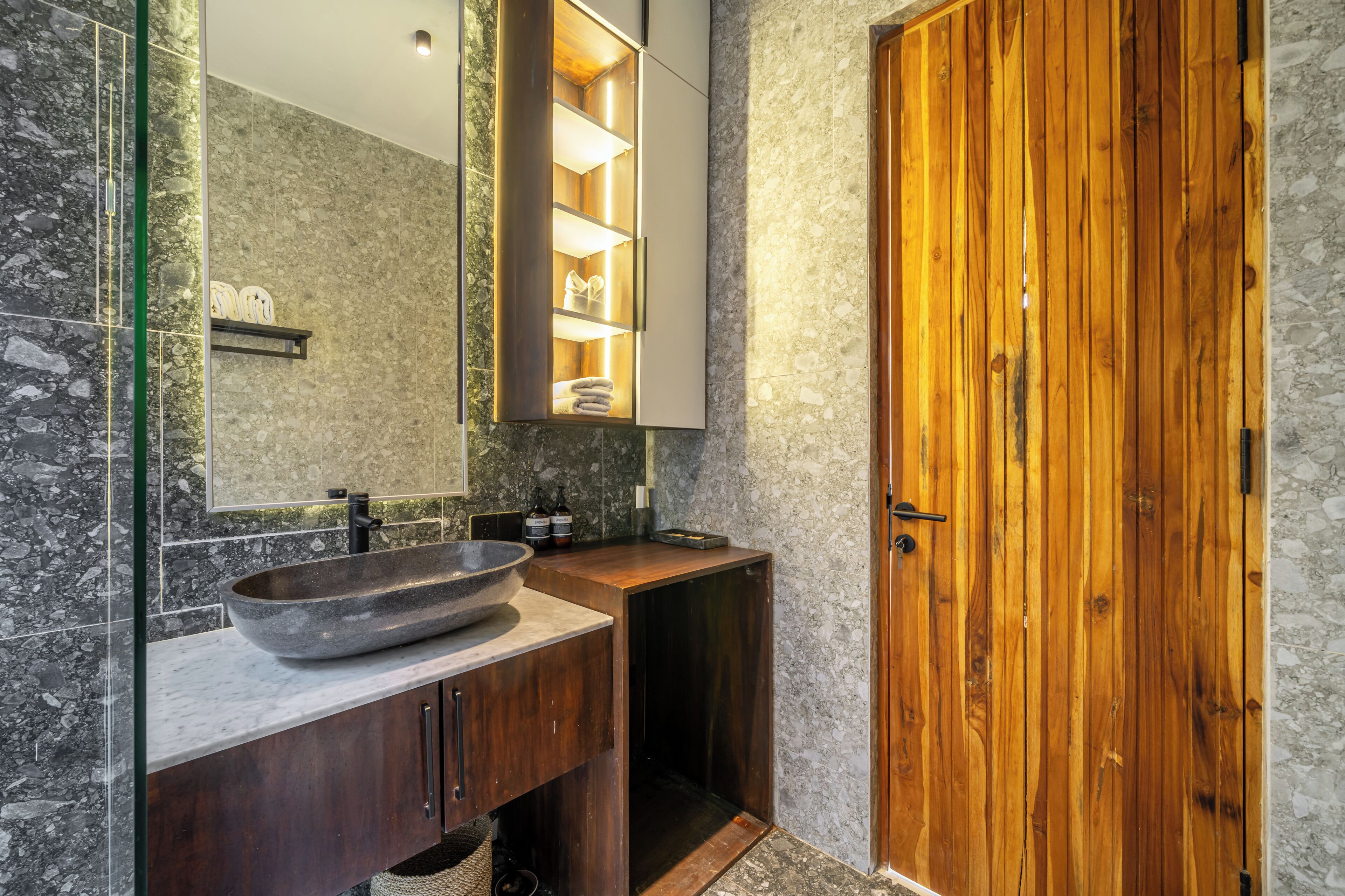 A bathroom with a large bowl sink, wooden vanity, and a wooden door.