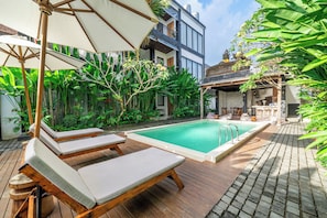 A pool area with lounge chairs and a wooden deck. - Sebelas Apartments Ubud (Gianyar)