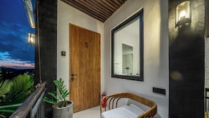 A modern room with a wooden door marked with the number 5, a large mirror, a bed with a wooden frame, and a potted plant. - Sebelas Apartments Ubud (Gianyar)
