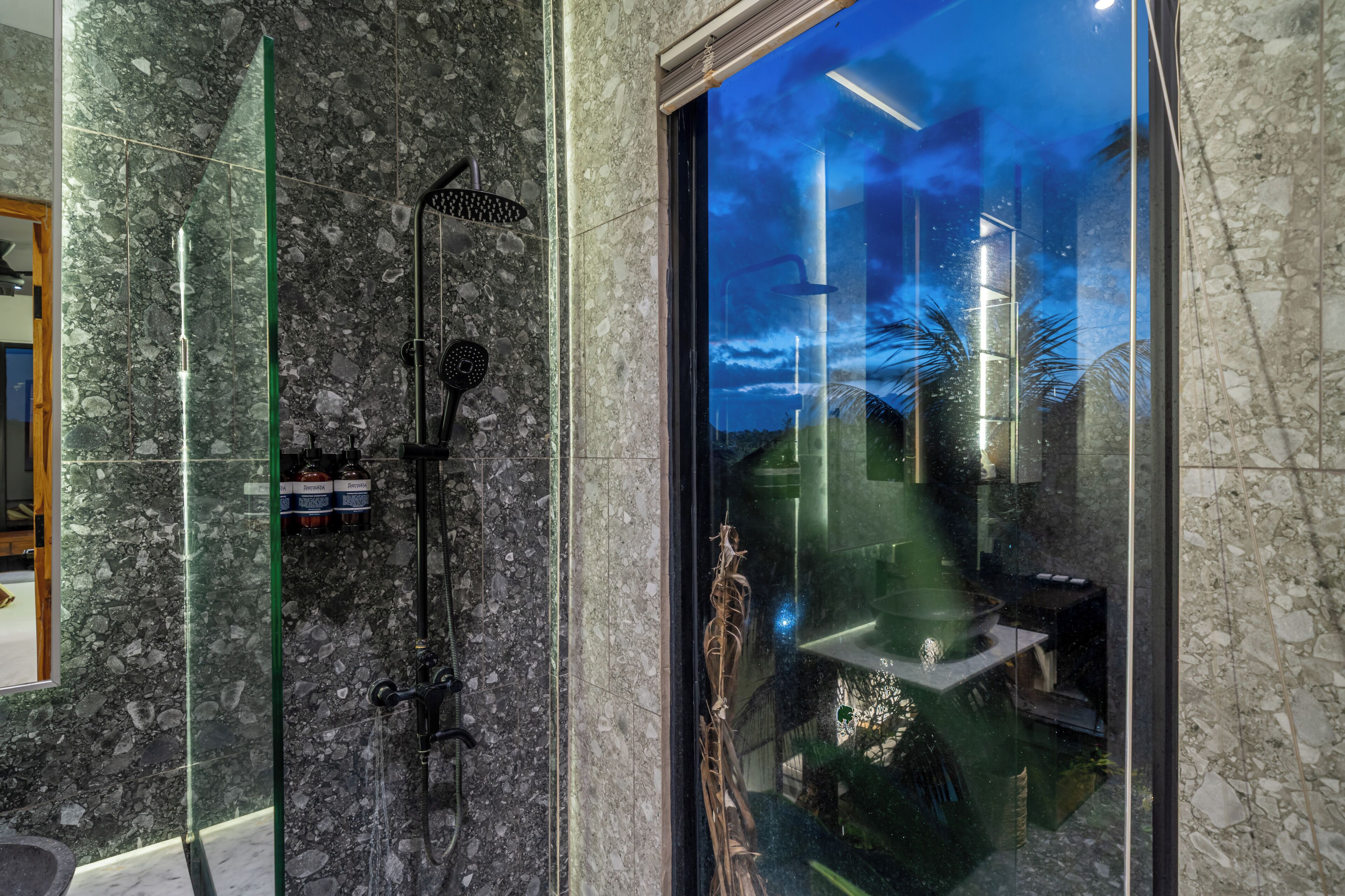 Un baño moderno con cabina de ducha de vidrio, una botella de champú a la vista y vistas al exterior a través del vidrio.