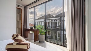 A modern hotel room with a large sliding glass door, a bed with a striped blanket, a desk, and a potted plant. - Sebelas Apartments Ubud (Gianyar)